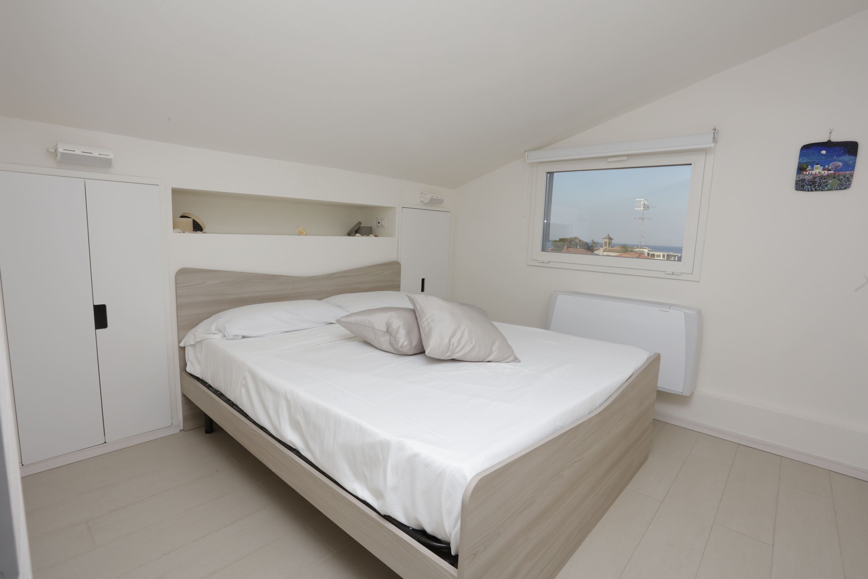 Ein Schlafzimmer mit einem Bett, einem Fenster mit Blick, einem Heizkörper und einem Kleiderschrank.