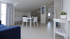Ein moderner, hell eingerichteter Raum mit Esstisch und Stühlen, einer Couch und einem kleinen Tisch mit Dekoration.