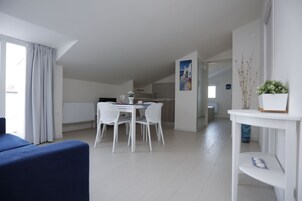 Una habitación moderna y bien iluminada con una mesa de comedor y sillas, un sofá y una mesita con objetos decorativos.
