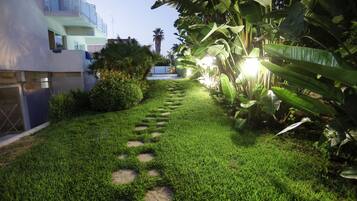 Un giardino curato con un vialetto in pietra, vegetazione rigogliosa e un edificio moderno con balconi.