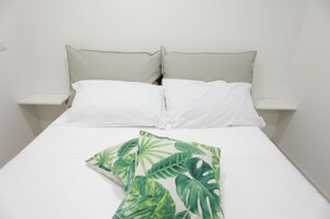 A bed with white linens, two pillows, and a tropical leaf-patterned throw.