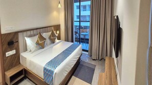 Hotellihuone, jossa on sänky, työpöytä, tuoli, televisio ja parveke, jossa on verhot.