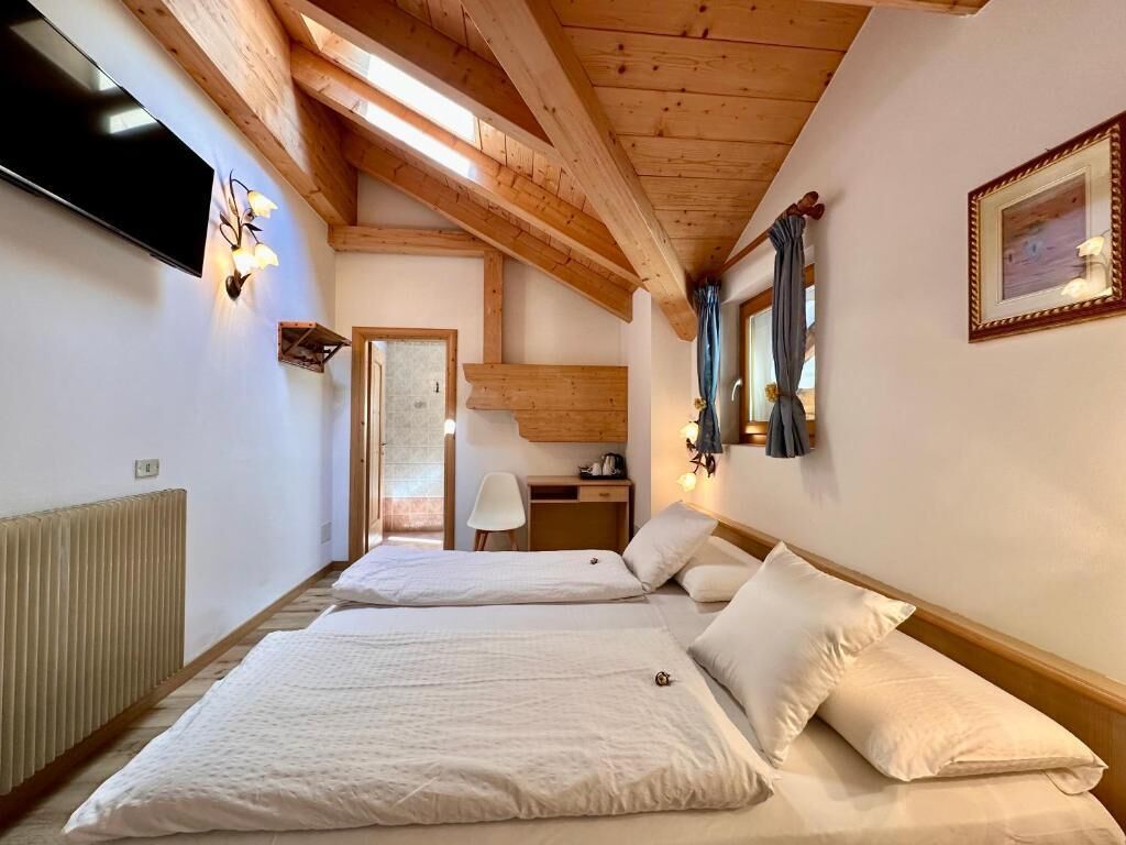 A room with two beds, wooden beams on the ceiling, a TV, a mirror, and a radiator.