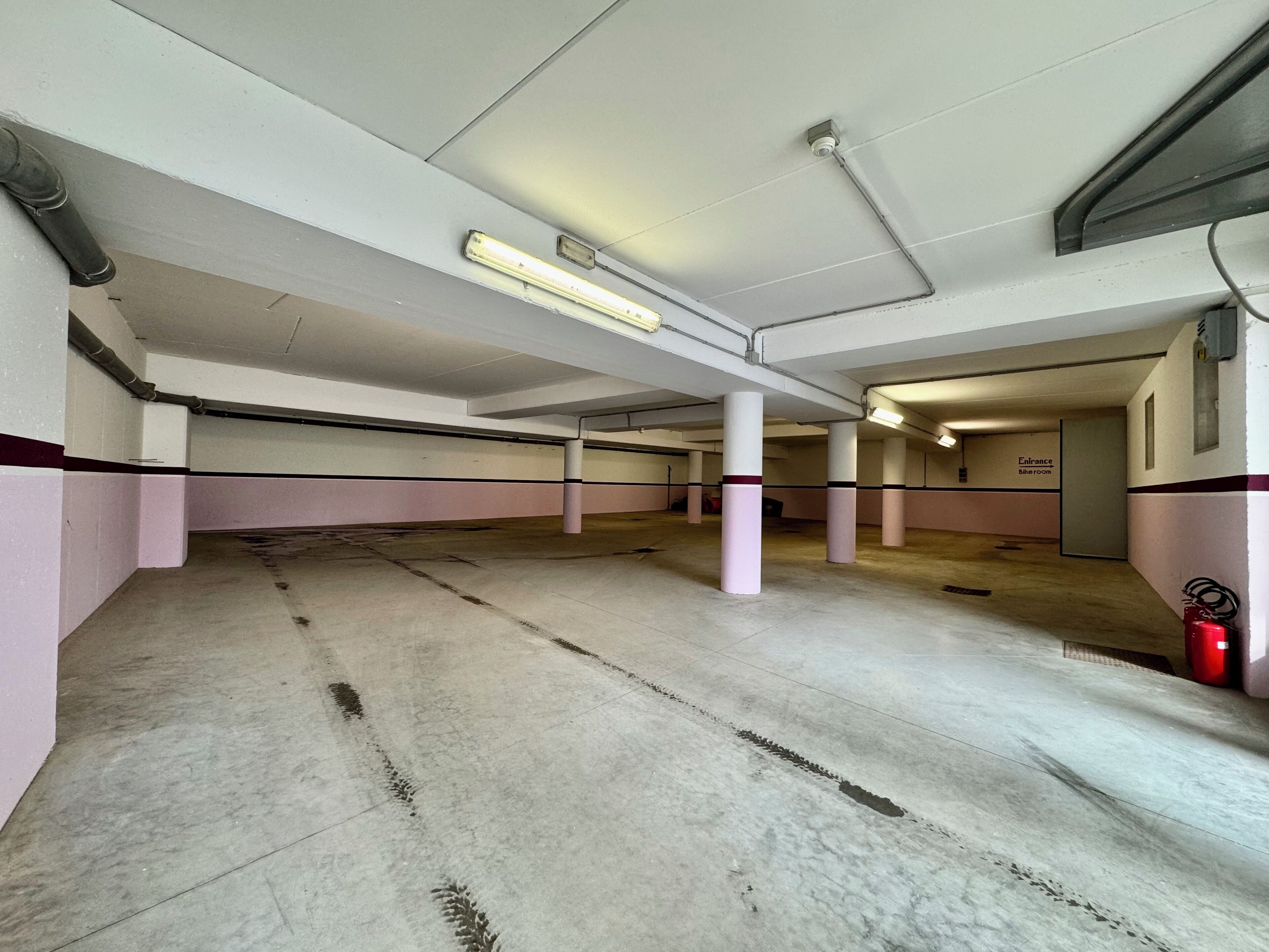 Eine überdachte Parkgarage mit Betonböden, Wänden in Weiß und Rosa sowie mehreren Säulen.
