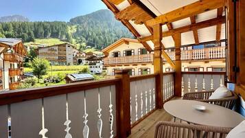 Un balcon offrant une vue sur un paysage montagneux, avec des balustrades en bois et une table entourée de chaises.