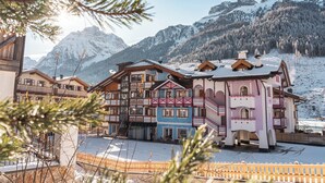 A multi-story hotel with balconies, a snow-covered ground, and mountains in the background.