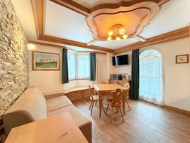 Una habitación acogedora con pared de piedra, techo de madera, una mesa de comedor con sillas, un sofá y un televisor montado en la pared.