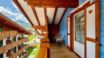 Un balcone in legno con vista su una montagna, una porta con decorazione a forma di cuore e una sedia.