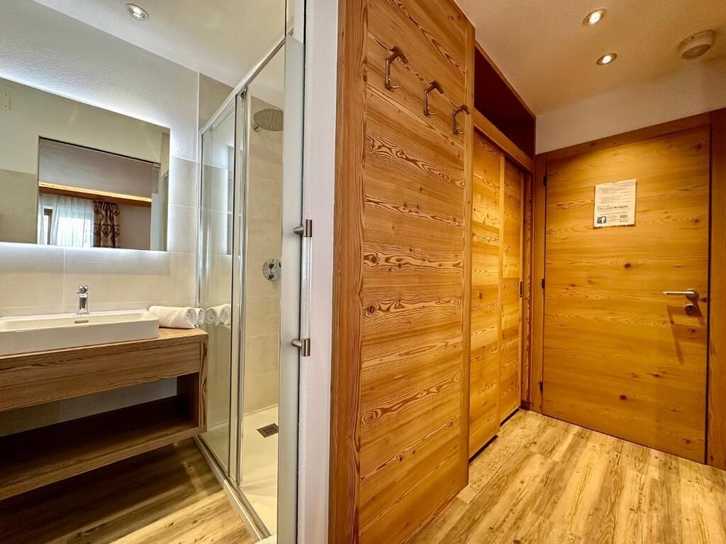 A bathroom with a glass shower enclosure, wooden panel walls, and a wooden door.