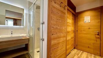 A bathroom with a glass shower enclosure, wooden panel walls, and a wooden door.