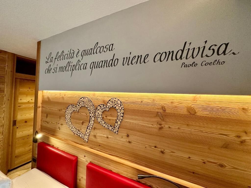 Una pared con una cita en italiano, un panel de madera con diseño de corazón y asientos rojos.