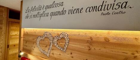 A wall with a quote in Italian, a wooden panel with a heart design, and red seating.