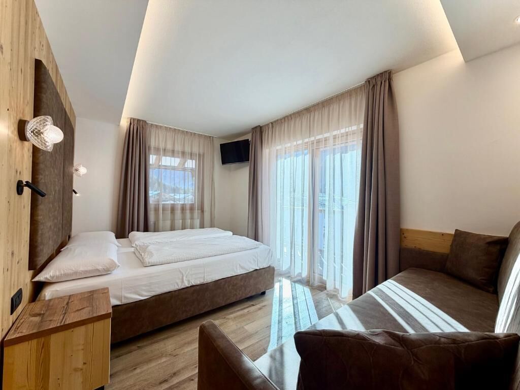 A modern hotel room with a bed, a sofa, a TV, and a wooden wardrobe.