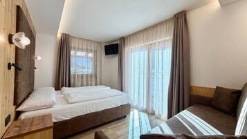 A modern hotel room with a bed, a sofa, a TV, and a wooden wardrobe.