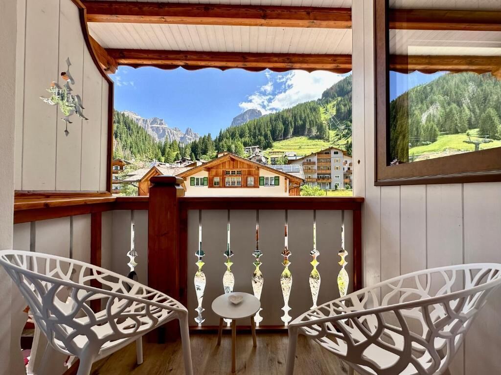 A balcony with two white chairs, a small table, and a view of a mountain village.