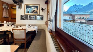 A dining area with a view of mountains, wooden furniture, and framed pictures on the wall.
