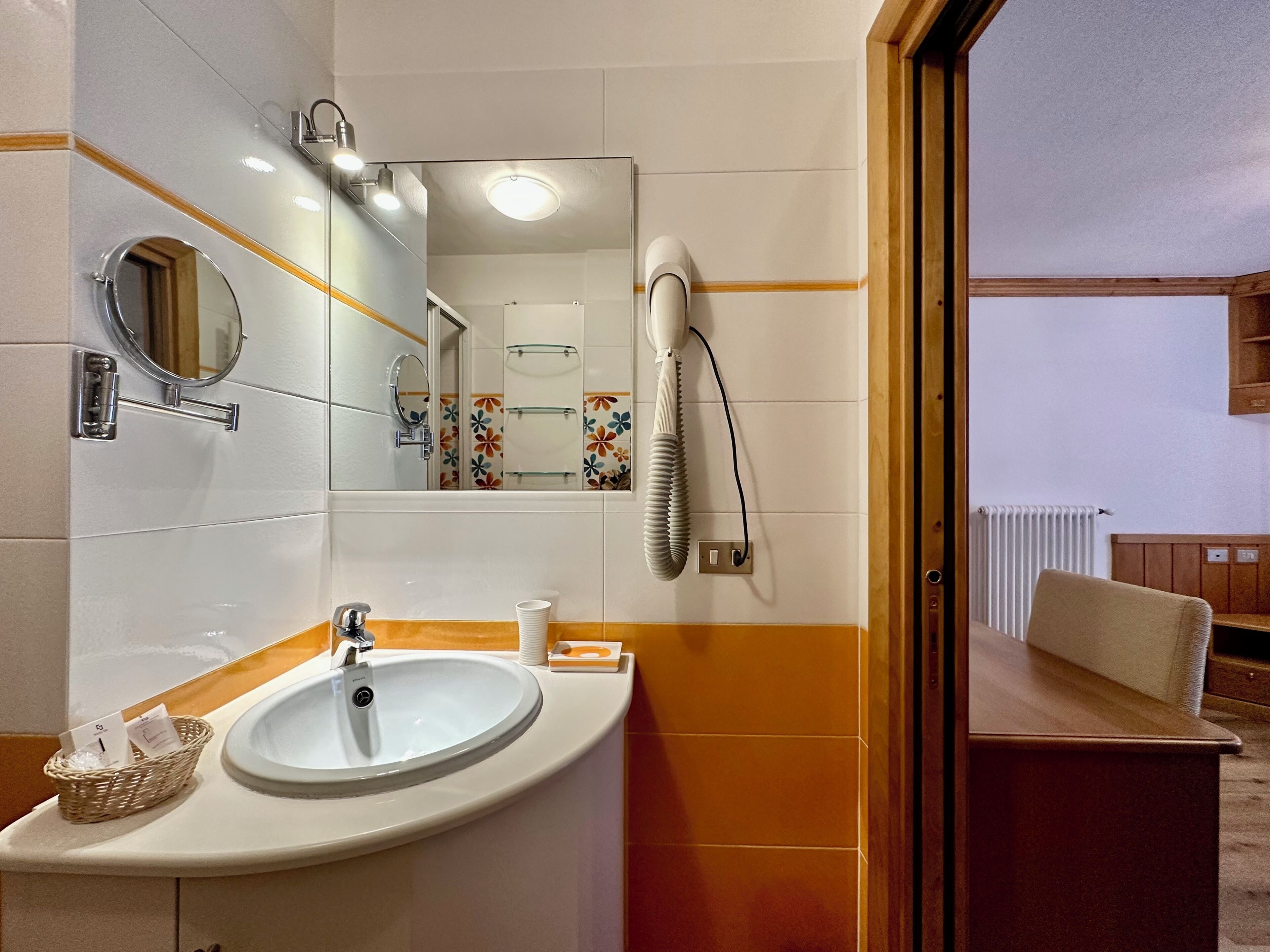 Un baño con lavamanos, espejo y secador de pelo montado en la pared.