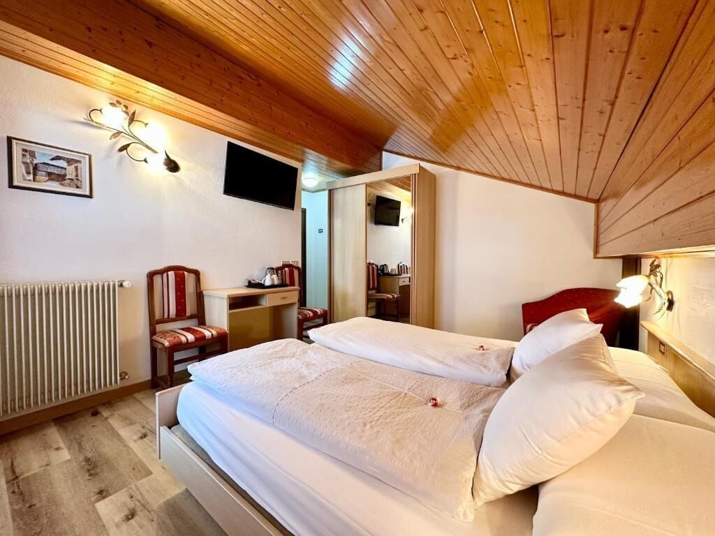 Een slaapkamer met een houten plafond, een bed met witte beddengoed, een stoel, een bureau en een radiator.