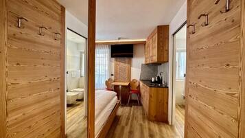 A compact room with a bed, a small desk, a toilet, and a kitchenette.