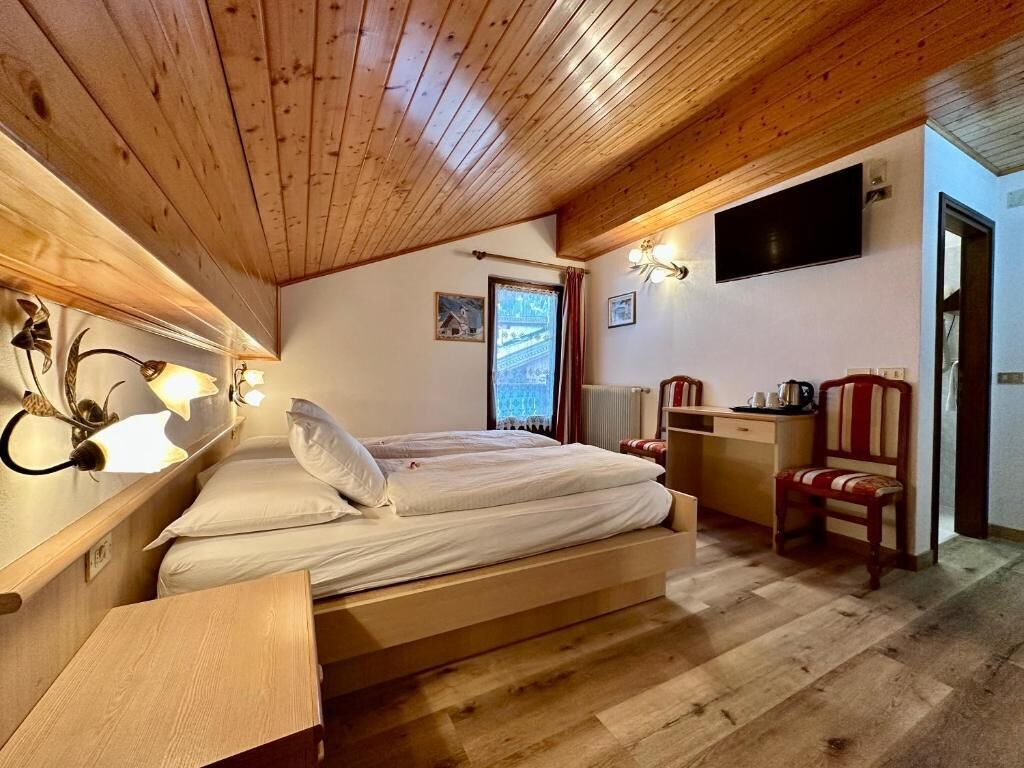 Un soffitto in legno, un letto con biancheria bianca, una scrivania con una sedia e un televisore montato a parete.