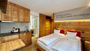 Una habitación de hotel moderna con cabecera de madera, cama con ropa de cama blanca, pequeña cocina y ducha.