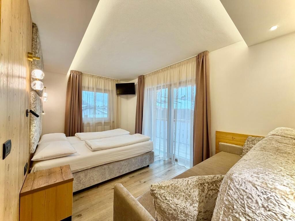 Ein Hotelzimmer mit Bett, Nachttisch aus Holz, Fernseher und einem Fenster mit Vorhängen.