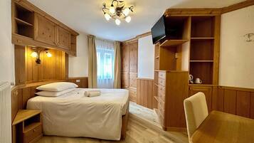 Een slaapkamer met een bed, een houten kledingkast, een bureau en een televisie.
