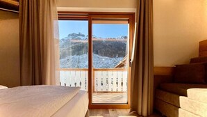 A room with a bed, a sofa, a view of a snowy landscape through a glass door, and a wooden floor.