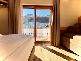 Una habitación con cama, sofá y vista a un paisaje nevado a través de una puerta de cristal, con piso de madera.