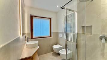 A modern bathroom with a glass shower enclosure, a large window, and a wooden vanity.