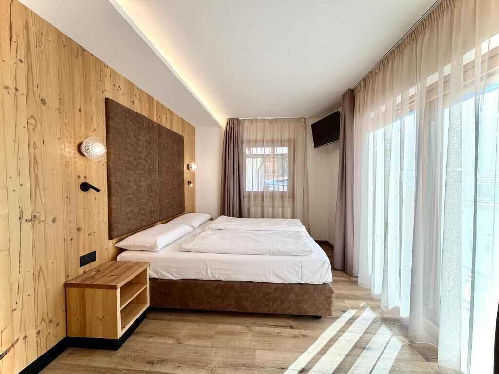 Camera d'albergo moderna con parete in legno decorativa, un grande letto, una TV a schermo piatto e una finestra con tende.