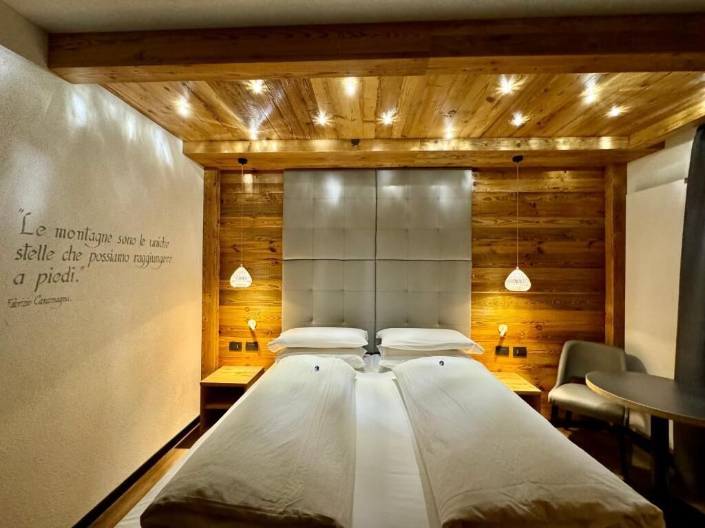Una stanza con un letto, una sedia e un tavolo. Sul muro, una citazione in italiano.