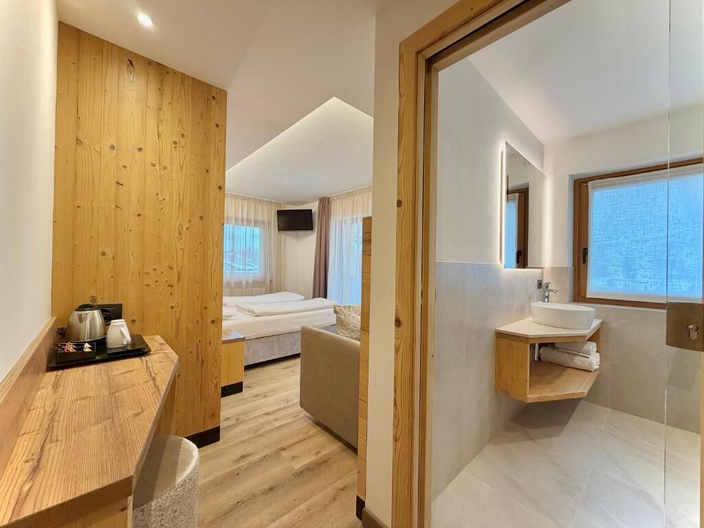 Una habitación de hotel moderna con una pared de acento de madera, una cama, un pequeño rincón de estar, un baño con lavabo y espejo, y una ventana.