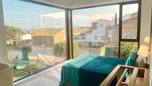A bedroom with a large window, a bed, a wooden chair, and a ceiling fan. - Chicos de Lastanosa 4 (Lastanosa)