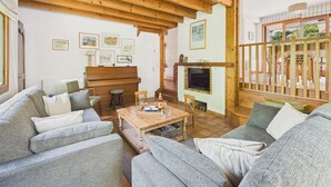 A cozy living room with a wooden ceiling, a fireplace, a piano, and a dining area. - House for 8, fenced garden, terrace & BBQ (Fouesnant)