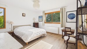 A bedroom with a bed, a desk, a chair, a radiator, and a window with curtains. - House for 8, fenced garden, terrace & BBQ (Fouesnant)