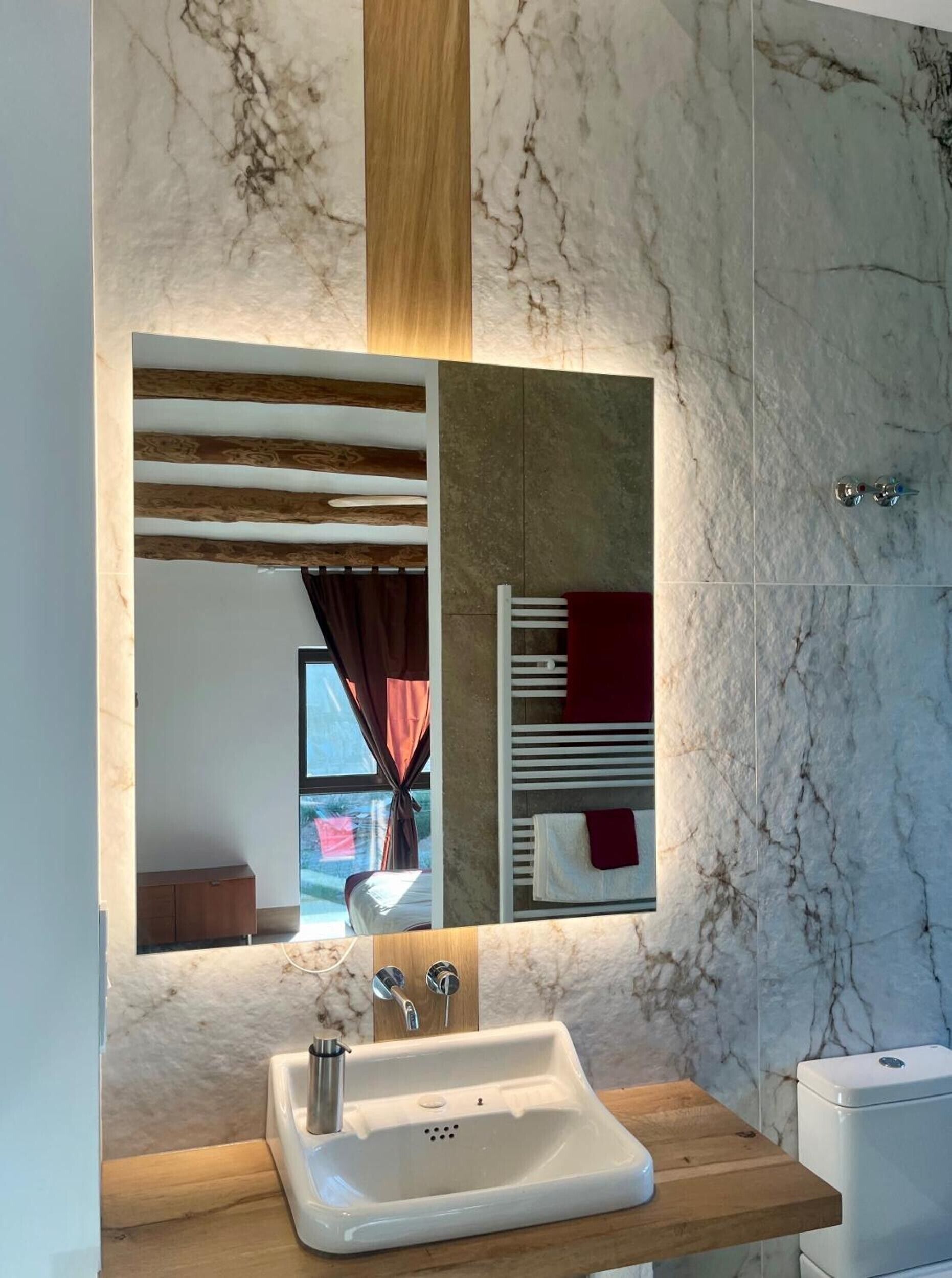 A bathroom with a marble wall, a wooden vanity, a sink, and a mirror.
