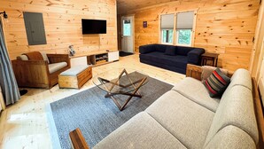 Un interno di una baita in legno con un divano, una TV, un armadio in legno e un tavolino da caffè in vetro.