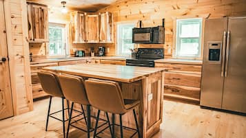 A wooden cabin-style kitchen with a central island, bar stools, a refrigerator, and a microwave.
