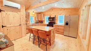 Interno di una baita in legno con angolo cottura, zona pranzo e un'ampia porta in legno.