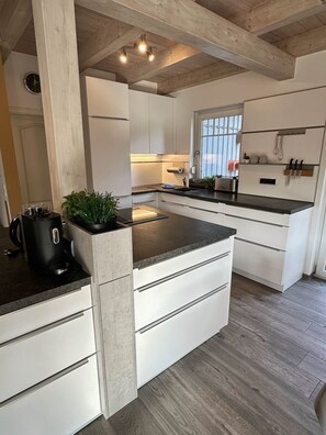 A modern kitchen with white cabinetry, a central island, and a wooden ceiling. - Brückelsee Chalet – Modern Holiday Home at Lake Brückelsee / Bavaria (Wackersdorf)