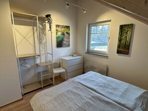 A bedroom with a bed, a window, a radiator, and artwork on the walls. - Brückelsee Chalet – Modern Holiday Home at Lake Brückelsee / Bavaria (Wackersdorf)