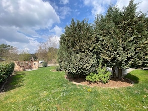 A well-maintained garden with a variety of trees and shrubs, a brick structure, and a clear sky.