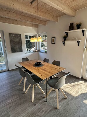 Een moderne eetruimte met een houten tafel, zwarte stoelen, een hanglamp en uitzicht op het omliggende landschap.
