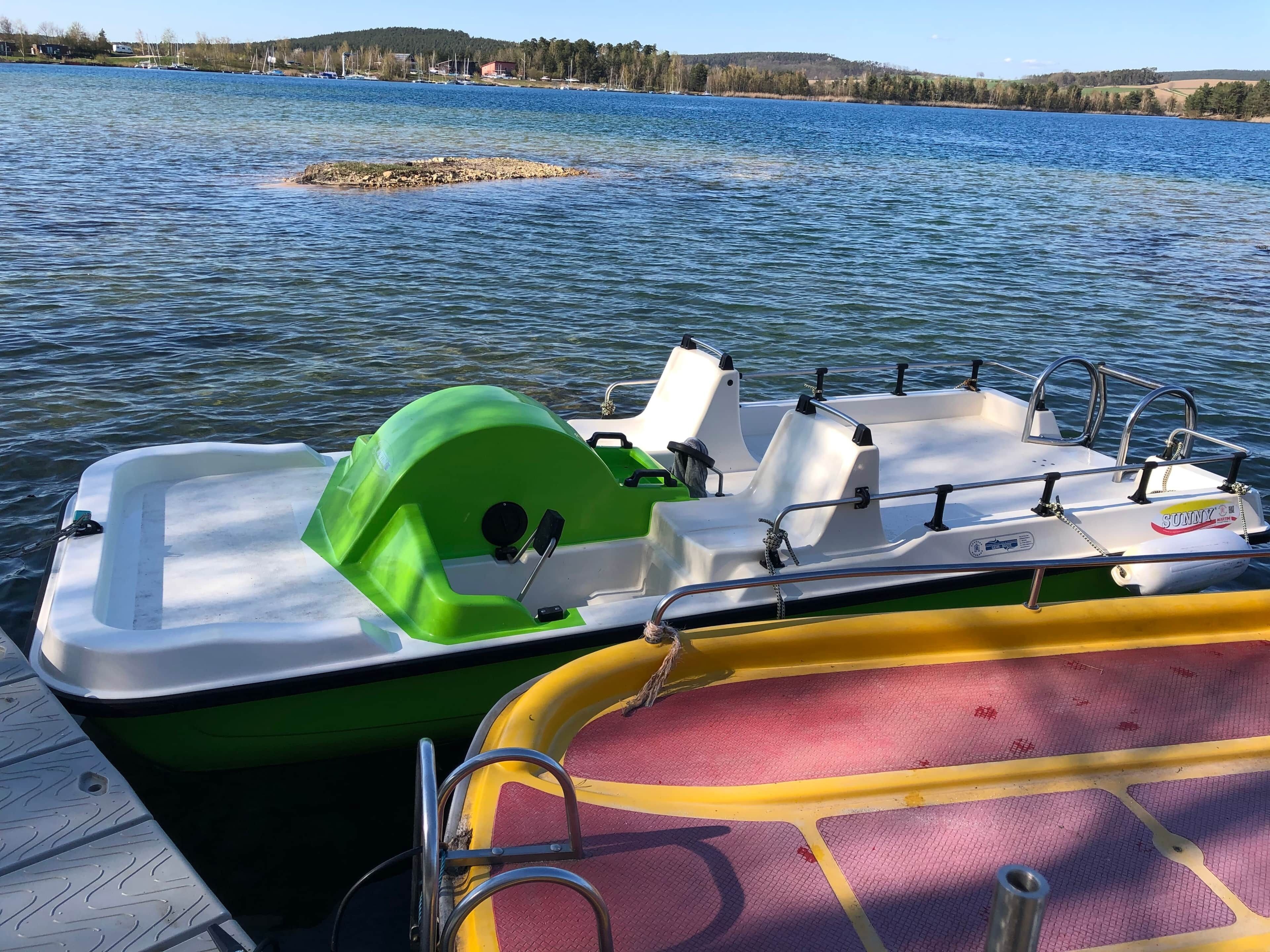 En båd ligger til kaj ved en bro med udsigt over et sø og en fjerntliggende kystlinje.