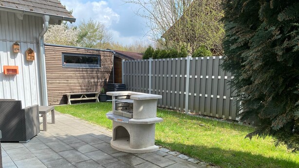 Eine Terrasse mit Steinfliesen, einem Stein-Barbecue und einem Holzzaun.
