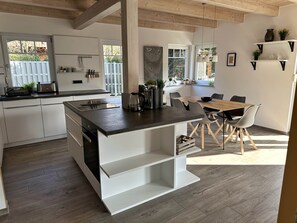 A modern kitchen with a central island, white cabinetry, and a dining area with a wooden table and chairs.
