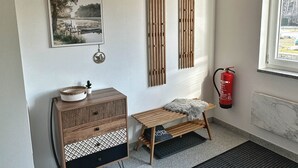 Ein Zimmer mit Holzboden, einem gerahmten Bild, einem kleinen Holztisch, einer Bank, einem Feuerlöscher und einem Fenster.