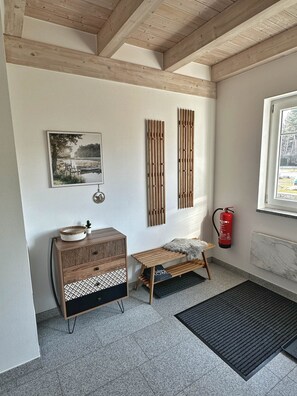 A room with a wooden ceiling, a framed picture, a small wooden table, a bench, a fire extinguisher, and a window. - Brückelsee Chalet – Modern Holiday Home at Lake Brückelsee / Bavaria (Wackersdorf)