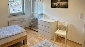 A bedroom with a bed, a desk, a chair, a wardrobe, and a window.